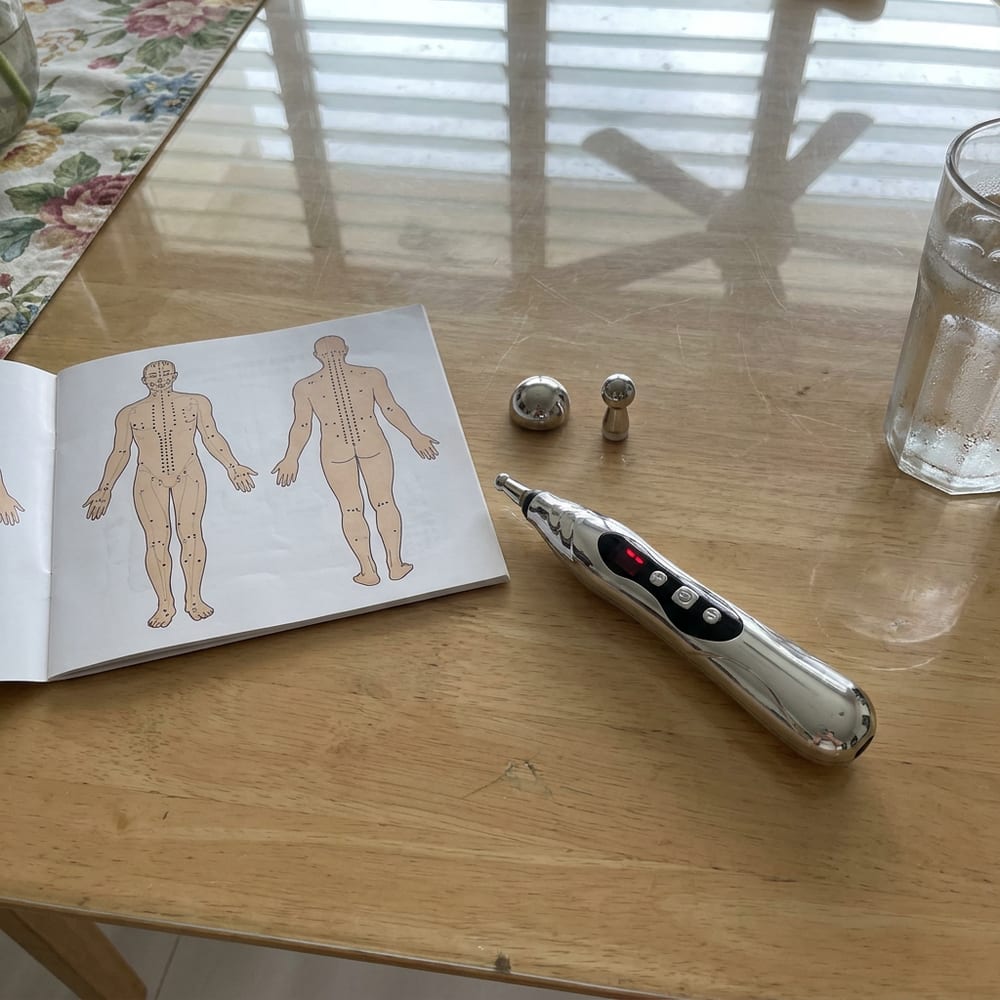 The PainFree Device pen with its dome and spherical heads next to the acupuncture point chart