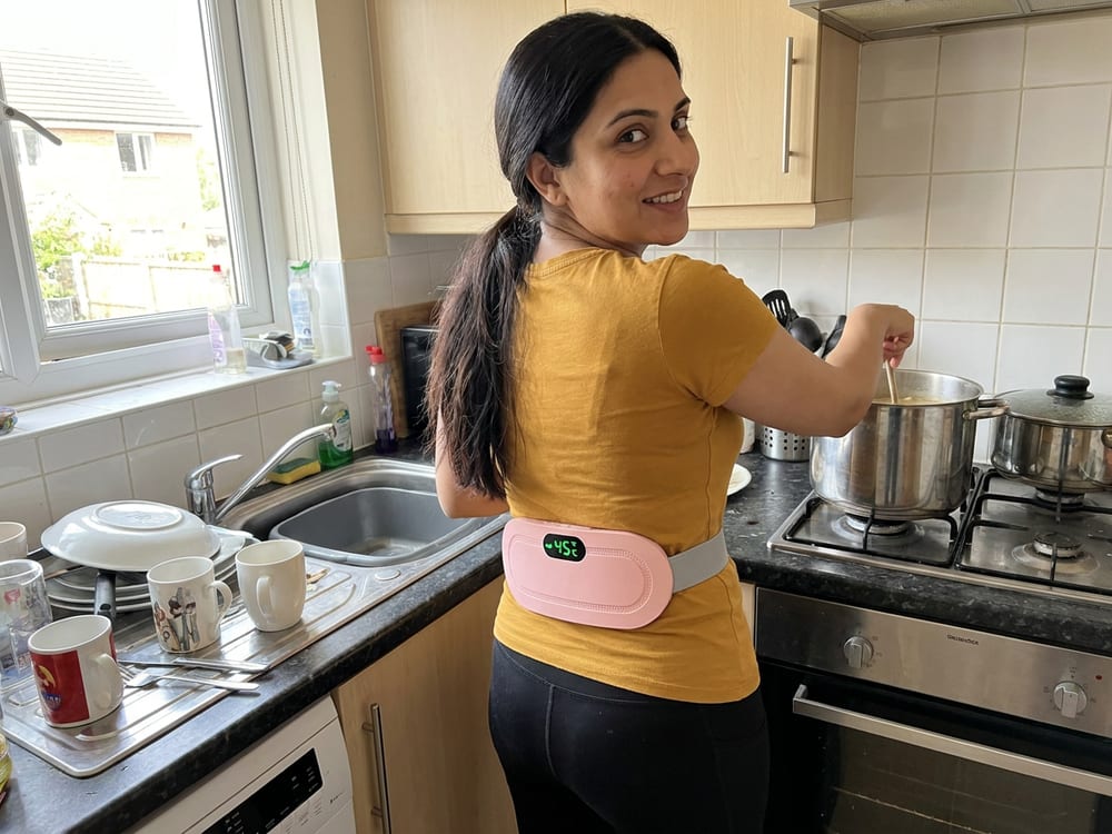 A woman walking around her kitchen wearing the heating belt on her lower back
