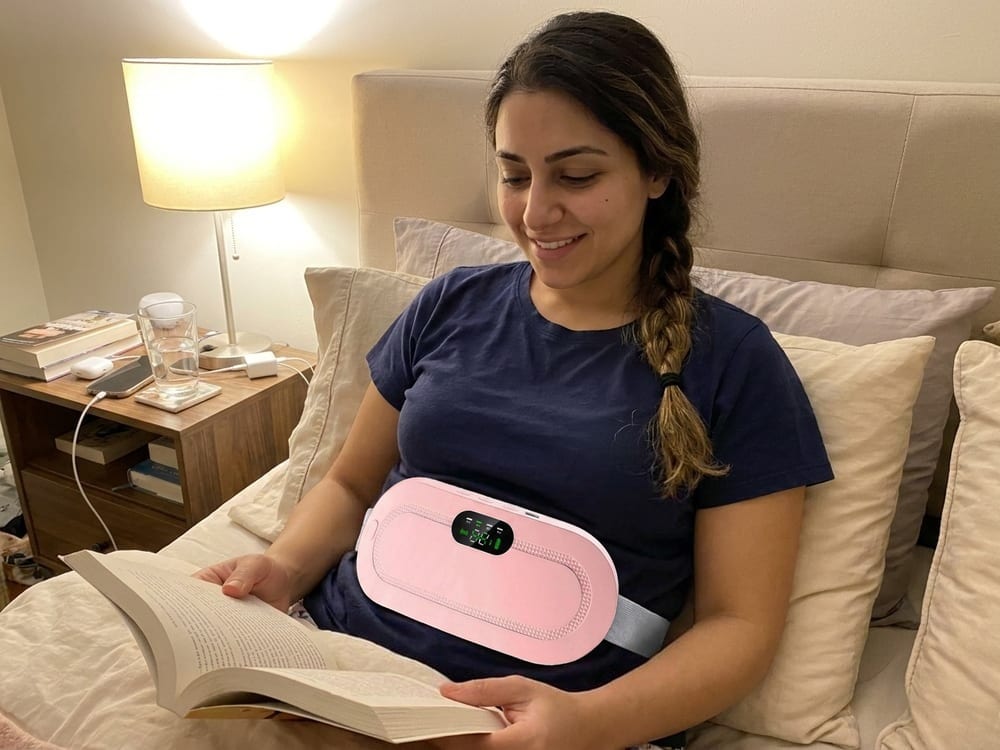 A smiling woman relaxing in bed wearing the heating belt