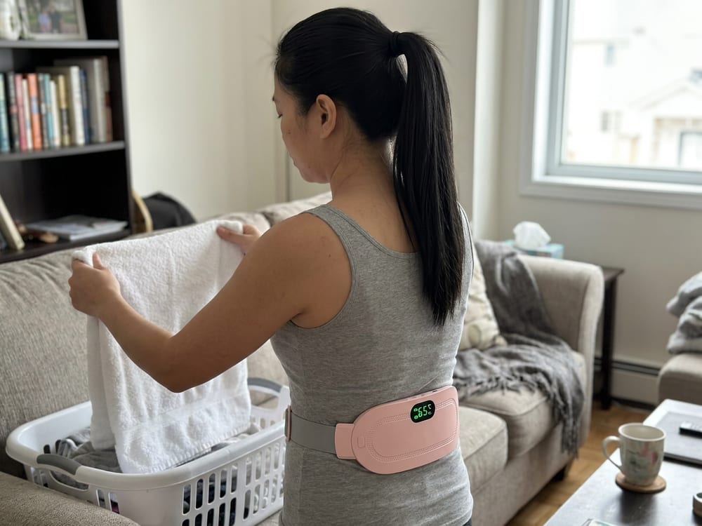 A woman folding laundry at home with the heating pad on her lower back