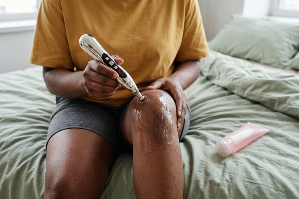 A woman gliding a silver electronic acupuncture pen over her lower back