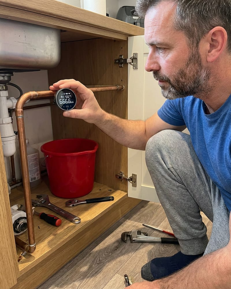 A man rolling the digital ruler along a curved pipe during a home project