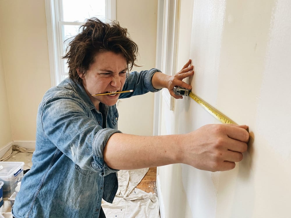 A person holding a tape measure in place with one hand and a pencil in their mouth