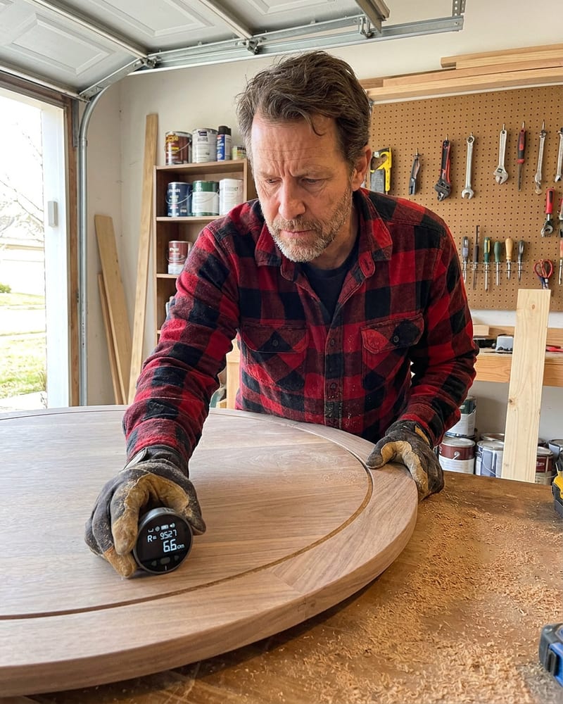 A maker rolling the Curvinch digital ruler along the curved edge of a round wooden tabletop in his workshop
