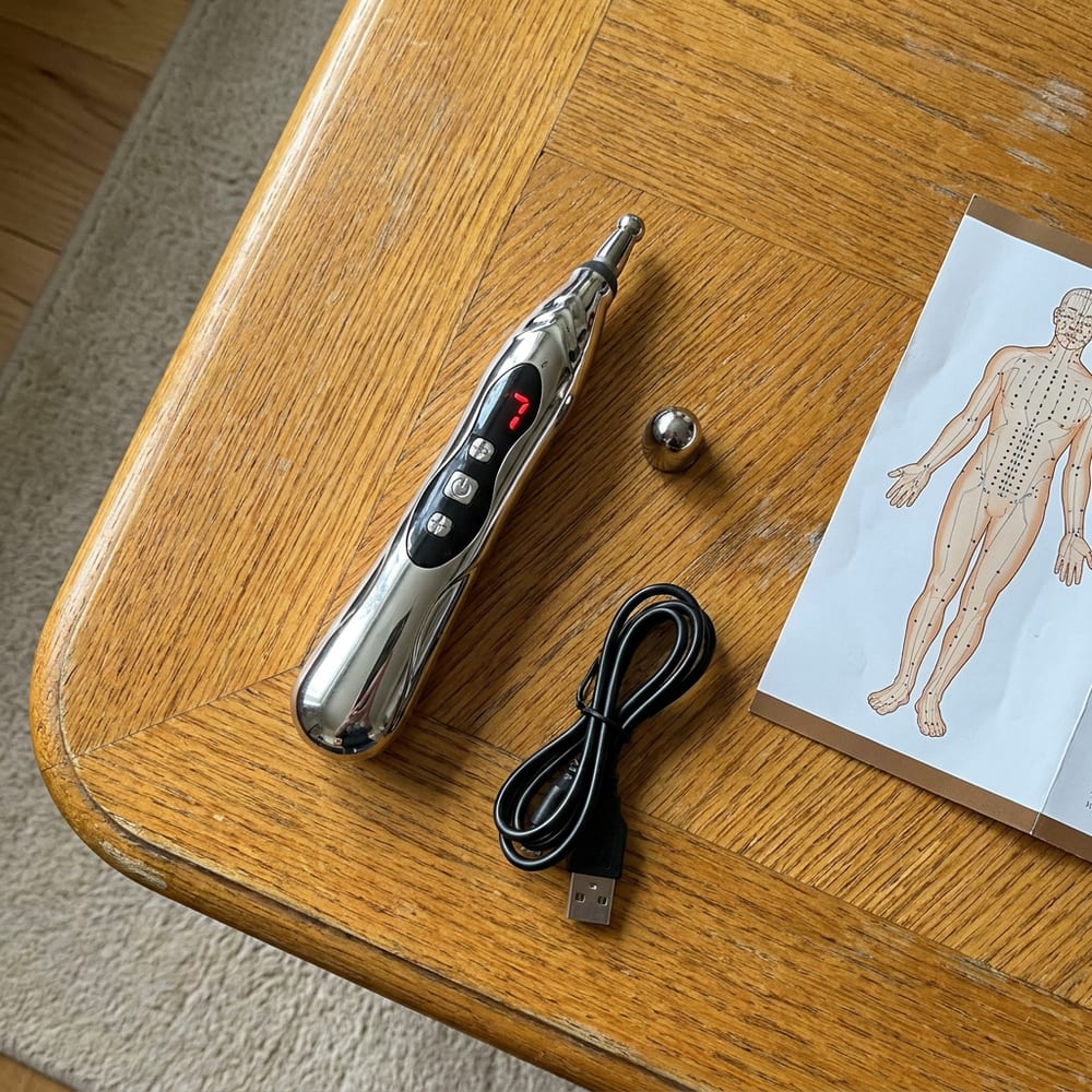 The PainFree Device pen with its heads, USB cable and acupuncture point chart on a windowsill